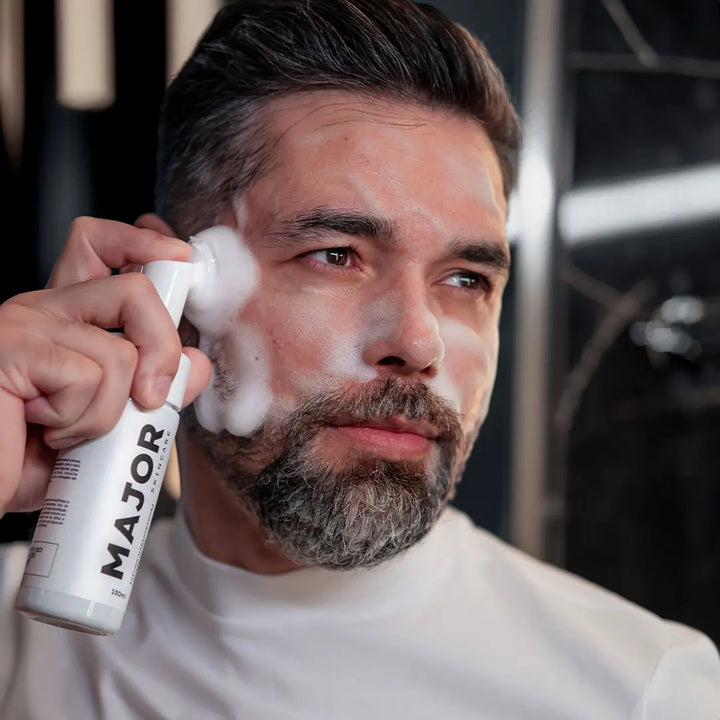 Homem aplicando espuma de limpeza profunda Major com escova massageadora no rosto.
