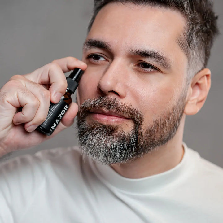 Homem aplicando sérum Major no rosto com expressão relaxada, segurando o frasco próximo ao rosto.