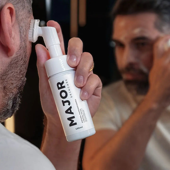 Homem aplicando espuma de limpeza facial Major no rosto em frente ao espelho, destacando cuidados com a pele masculina