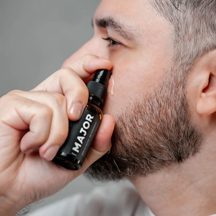 Homem aplicando sérum Major no rosto, borrifando o produto diretamente na região das bochechas.