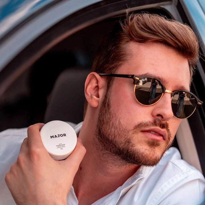Homem estiloso segurando pomada modeladora Major para cabelo masculino, finalização efeito matte seco, fixação profissional e estilo moderno.